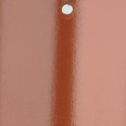Billedet viser et vertikalt område af en væg, som er malet med tagmaling i en terrakotta nuance. Billedet fokuserer på en stripe, hvor en nyere og muligvis friskere lag maling fremviser en mere intens og dyb farve sammenlignet med den omkringliggende overflade. Der er også en synlig dråbeformet aftegning eller et hul nær toppen af den tydelige stribe, hvilket bryder ensartetheden i malingslaget. Dette billede illustrerer farveforskellen, som kan opstå, når tagmaling påføres i flere lag eller over tid. Søgeordene for dette billede ville være 