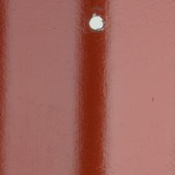 Billedet viser en overflade malet med tagmaling i en nuance af rød. Overfladen ser jævn og ensartet ud med en svag glans. Midt i billedet ses en skinnende hvid prik, som kunne være refleksion fra en lyskilde, der rammer en skrue eller et andet rundt, fladt objekt fastgjort til overfladen. Farven på malingen giver et robust og holdbart indtryk, ideelt til et tag, der skal stå imod vejr og vind.